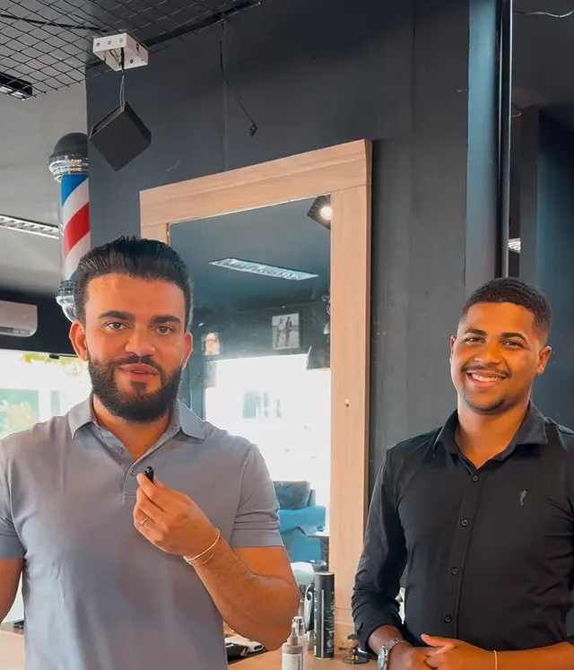 Cliente e barbeiro no salão, ao lado do poste de barbearia